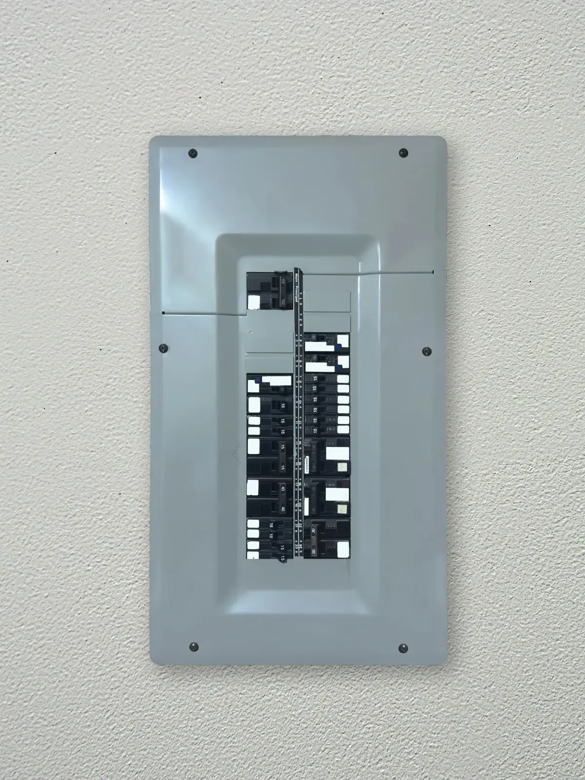 A gray electrical breaker panel on a textured, off-white wall. The panel is closed with no visible text or actions occurring.